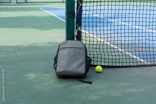 Backpacks and tennis balls are placed on the tennis court floor