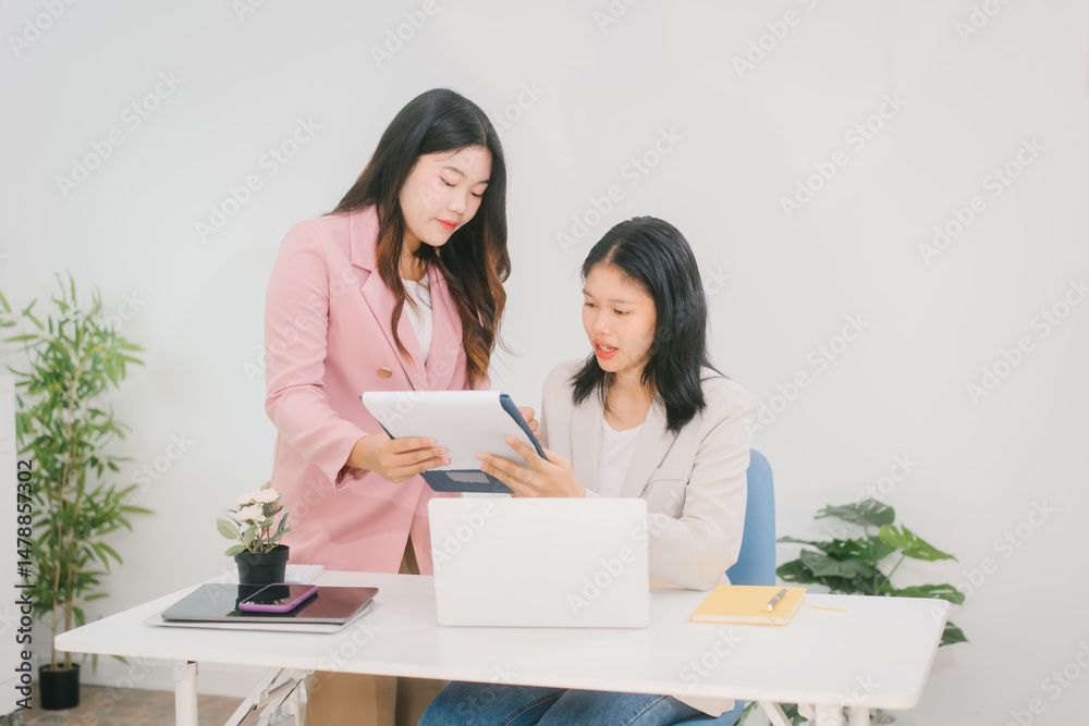 Two Asian businesswoman are engaged in a productive discussion at a modern office table, using a laptop and documents, exchanging ideas, and working together in a bright, professional environment Two Asian businesswoman are engaged in a productive discussion at a modern office table, using a laptop and documents, exchanging ideas, and working together in a bright, professional environment