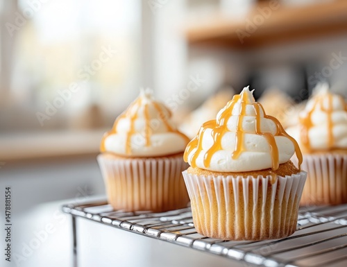 Freshly baked cupcakes, drizzled with caramel, sit on a cooling rack.  Close-up view, soft focus