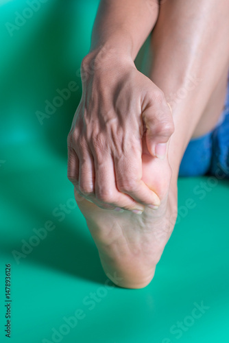 Close up of woman's foot with ankle pain on green background.