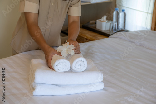 Hands of hotel maid putting plumeria flower and towels on the bed in the luxury hotel room ready for tourist travel
