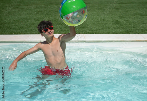 Young boy having fun playing with inflatable ball in swimming pool on sunny summer day with copy space