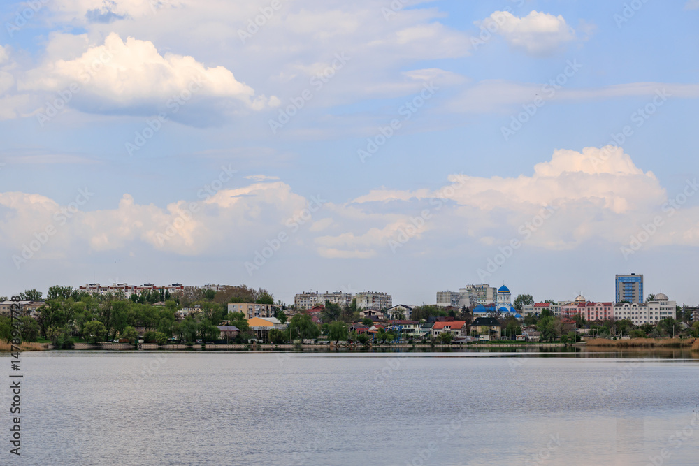 Obraz premium Scenic lakeside cityscape with urban buildings under fluffy clouds