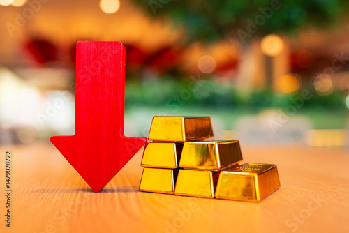 Φωτογραφία Gold bars and red arrow pointing down placed on the table, concept of gold price is decreasing due to going up high