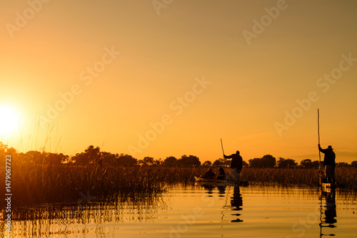 Two Makoros (also spelt mekoro, mokoro) with tourists gliding along one of the channels in the Okavango Delta at sunset. Botswana.