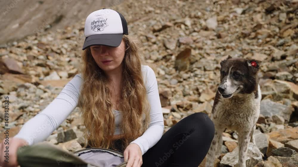 custom made wallpaper toronto digitalYoung woman rests on hiking trail with dog asking for snack. Searches backpack, finds food for pet. Rock-strewn path, outdoor adventure. Daytime scene with pet companion, mountain backdrop. Slowmo