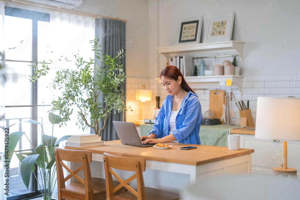 A casual relax young woman is looking at a laptop in the kitchen at home Smiling young female entrepreneur working on a laptop A casual relax young woman is looking at a laptop in the kitchen at home Smiling young female entrepreneur working on a laptop