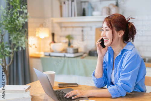Asian adult Woman working from home in kitchen Beautiful young woman with an amputated arm working on a laptop and talking on a smartphone Woman Using Laptop At Home