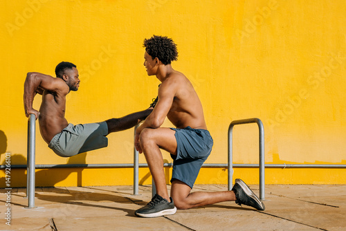 Young men engage in outdoor workout session demonstrating strength and fitness techniques against vibrant yellow backdrop