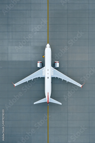 Aerial view of a passenger jet parked on the tarmac. White fuselage, red wingtips and tail. Ground markings with a yellow line guide the aircraft.