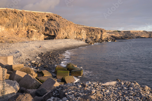 Picturesque rocky pebbles beach with stones wall in Playa de San Juan. Playa de San Juan is a small fishing village on the south west of Tenerife island. Golden hour light