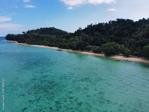 Breathtaking aerial view of crystal-clear turquoise water gently washing a pristine sandy beach, backed by vibrant green tropical rainforest in Thailand, Ko Kradan, Trang photo