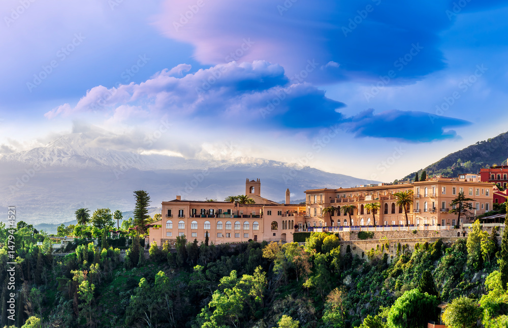 Fototapeta premium Amazing landscape of a beautiful mountain town Taormina in Sicily, Italy. Scenic view from a green mountain to a beautiful famous hotel and high majestic mount vulcan Enta in snow.