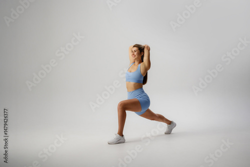 Female athlete performing a forward lunge in a light blue workout set on a neutral background