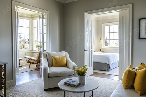 Bright modern living room interior with elegant white furniture, yellow accent pillows, large windows and classic French paneling. Natural light and fresh flowers. Sophisticated and cozy touch.
