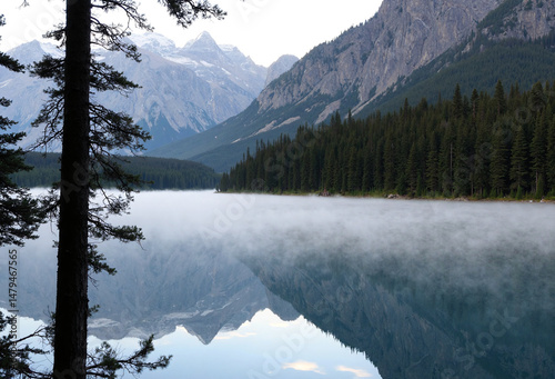 A serene lake reflects towering mountains and a dense forest under a misty sky, creating a picturesque landscape - Generative AI