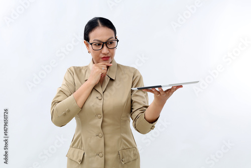 Asian civil servant woman standing holding a computer tablet, thinking and looking at tablet. Technology concept
