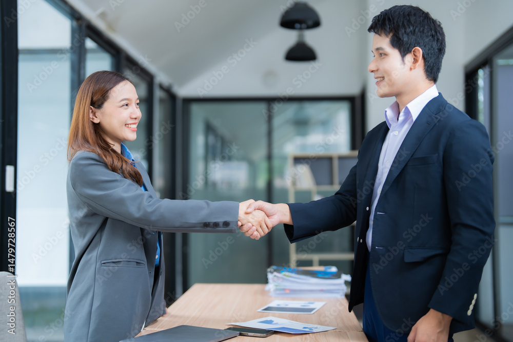 Fototapeta premium Two asian businesspeople in suits shaking hands after reaching an agreement during a meeting in a modern office, showing trust and cooperation
