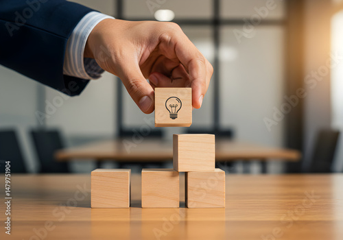 A businessman strategically places a wooden block with a lightbulb symbol atop a growing stack of blocks symbolizing innovative ideas business growth and strategic planning in a modern office setting photo