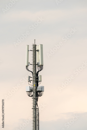Cellphone mast with aerials and  cabling. Installation. Cloudy, but bright sky. Vertical shot. .