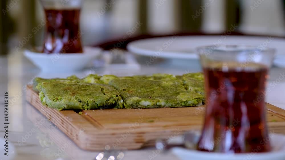 Traditional Turkish dessert Katmer with clotted cream and dough served with tea on a restaurant table. Prepared with thin dough, green ground pistachio and sherbet. Dessert of Gaziantep region.