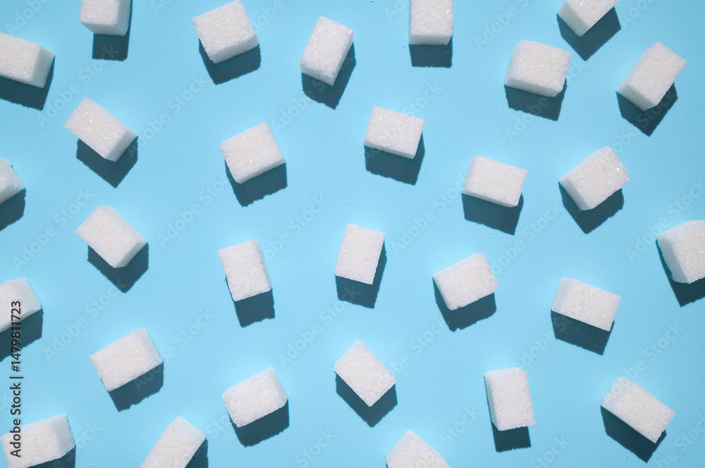 White sugar cubes on blue background top view flat lay. Scattered sugar cubes. Abstract pattern of food. Concept of sweets consumption and addiction, global issue of health 