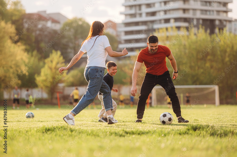 Obraz premium Running, playing soccer. Family of mother, father and son are playing on the field