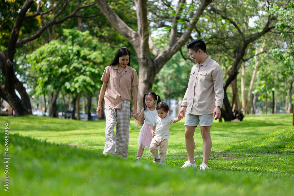 Obraz premium Happy family walking together in a sunny green park, each parent carrying a child.