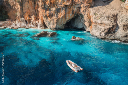 Aerial view of boats near cliffs on blue sea on sunny day in summer. Cala Goloritze, Sardinia, Italy. Aerial view of sea lagoon, shore, transparent water, rocks, beach. Top drone view. Seascape