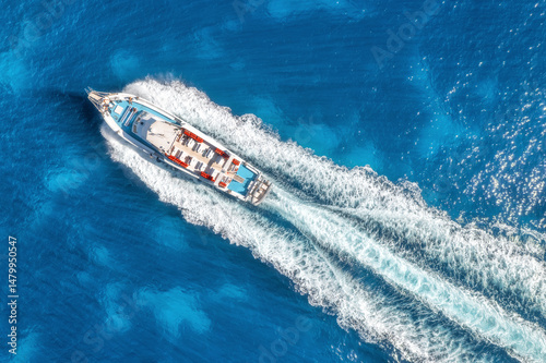 Aerial view of beautiful floating yacht in blue sea on sunny day in summer. Sardinia island, Italy. Top drone view of speed boat, sea coast, transparent water. Travel. Tropical landscape. Yachting