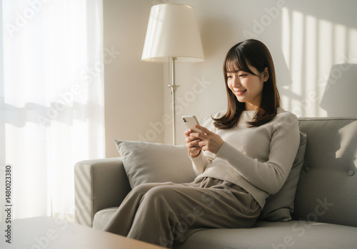 ソファでスマートフォンを操作する若い女性