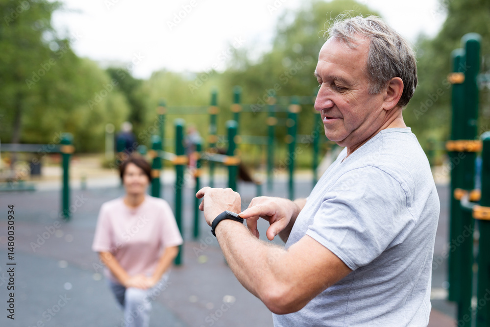 Elderly man looking at his smart bracelet in open-air sports area