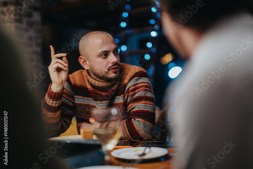 A bald man in a colorful sweater engages in a lively conversation with friends around a table inside a warmly lit setting, creating a cozy and inviting atmosphere.