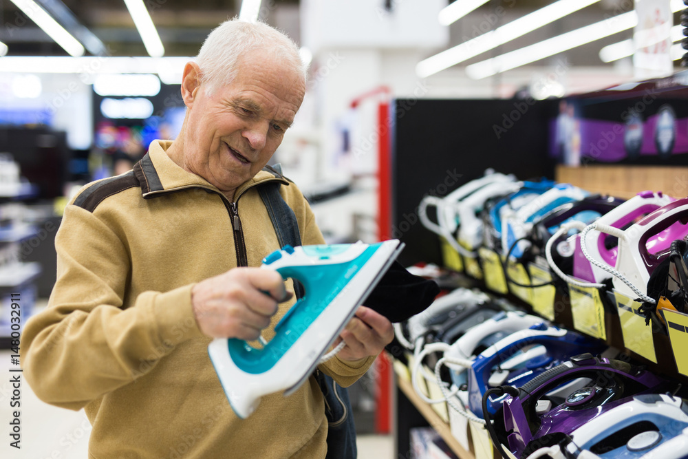 Senor man pensioner buying iron in showroom of electrical appliance store