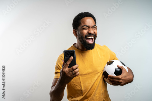 Handsome happy excited African man celebrating in euphoria mood after winning a bet, holding a smartphone in hand, isolated studio background.