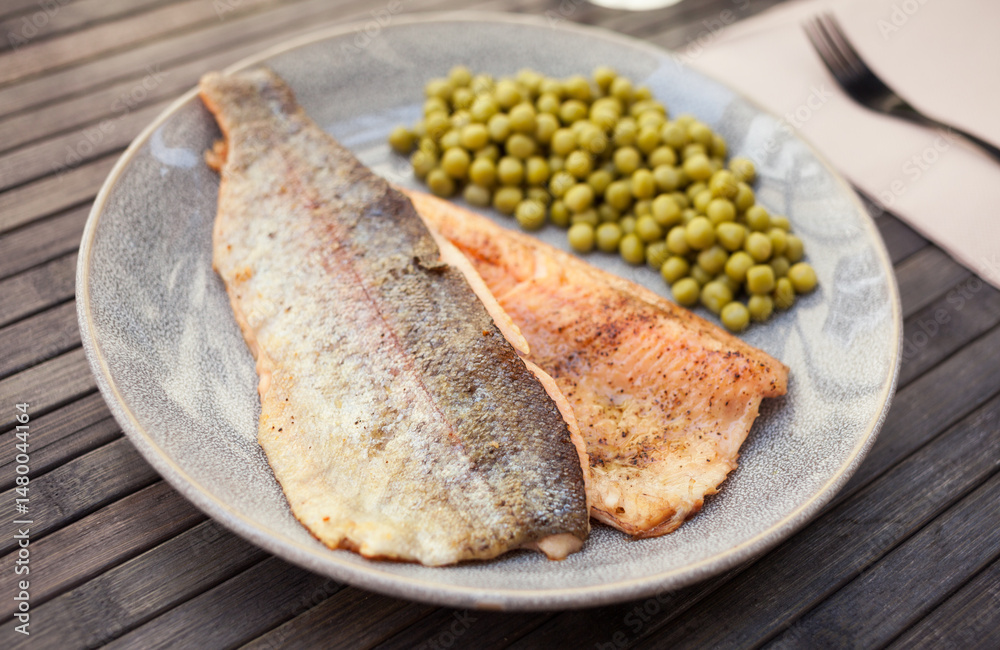 Top view of baked trout fillet served on plate with peas closeup
