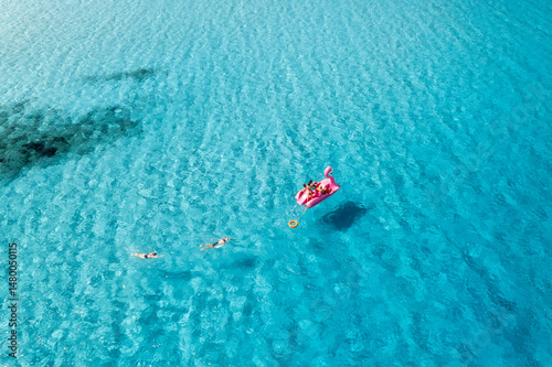 Fototapeta Naklejka Na Ścianę i Meble -  Aerial view of Inflatable pink flamingo with people on crystal clear blue water on summer sunny day. Top drone view of relax family on boat, azure sea in Sardinia Island, Italy. Travel and vacation