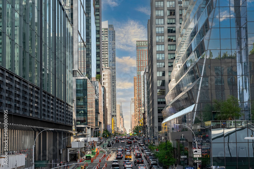 City street with tall buildings and heavy car traffic. A cloudy sky with some blue patches above the skyscrapers in an urban environment.