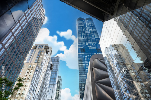 Cityscape View: A modern architectural landscape of towering skyscrapers reaching up to a blue sky with scattered clouds on a bright sunny day.