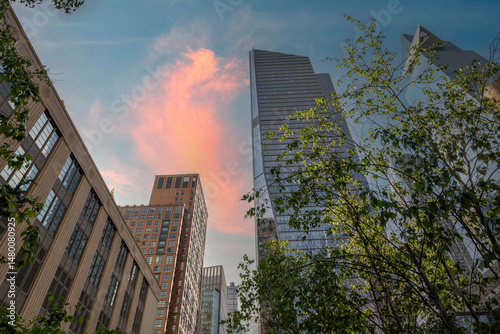 City skyline featuring modern architecture reaching towards a vibrant, colorful sky, framed by lush greenery.