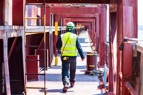 A port employee, stevedore,  walking across the deck of a merchant ship during his daily routine activities on board of the large container ship.