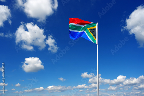 flag of South Africa fluttering in the blue sky with cumulus clouds