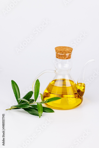 Healthy olive oil in glass bottle with fresh branch on white backdrop