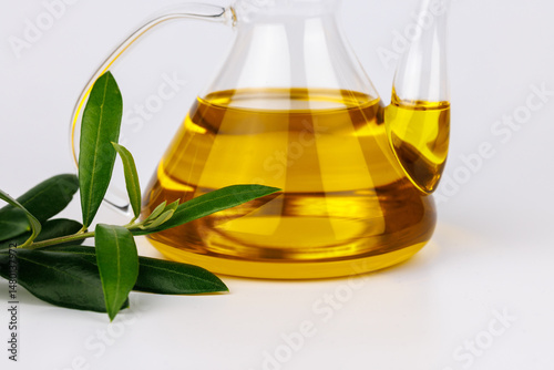 Glass oil dispenser with olive oil and twig on isolated white background