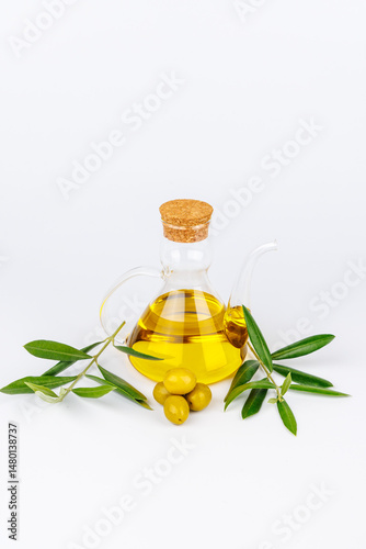 Clear olive oil cruet and green olives with olive twigs on white backdrop, natural food photography