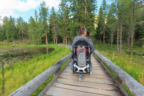 Person using wheelchair navigates accessible trails in the Dolomites surrounded by lush greenery in Italy. The serene landscape offers a peaceful experience in nature.