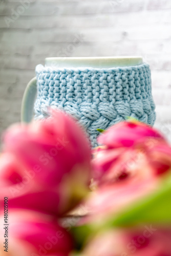Pink tulips blurred foreground, open book and a mug of freshly brewed coffee or tea. Spring set