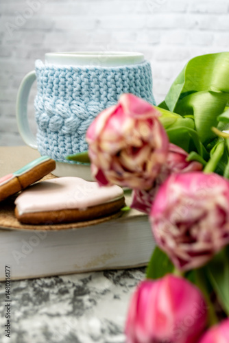 Pink tulips blurred foreground, open book and a mug of freshly brewed coffee or tea. Spring set