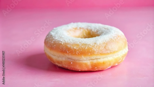 A close-up of a single donut dusted with powdered sugar, sitting on a soft pink background, a sweet and simple treat