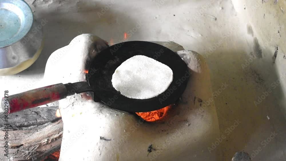 Video clip of chapati or roti being cooked on a flat iron tawa over a traditional clay stove or chulha in an Indian village . Indian cuisine, village lifestyle, traditional cooking methods concept.